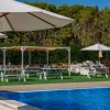 Una piscina con ombrelloni bianchi e tavoli da picnic su un prato verde circondato da alberi.