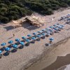 Una spiaggia con ombrelloni blu allineati e un chiosco di legno nella sabbia.
