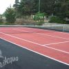 Campo da tennis con superficie rossastra e rete centrale.