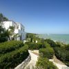 Una casa bianca immersa nel verde con vista sul mare e il cielo azzurro.