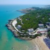 Vista aerea di una costa con spiaggia, ombrelloni colorati e vegetazione rigogliosa.