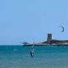 Windsurfista e aquilone in mare, torre sullo sfondo.