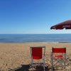 Sedie e ombrellone rossi su spiaggia sabbiosa.