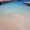 Spiaggia con sabbia chiara e mare azzurro, incorniciata da rocce.