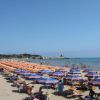 Spiaggia con ombrelloni arancioni e blu, mare calmo e torre in lontananza.