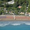 Veduta aerea di una spiaggia con ombrelloni colorati e case tra gli alberi.