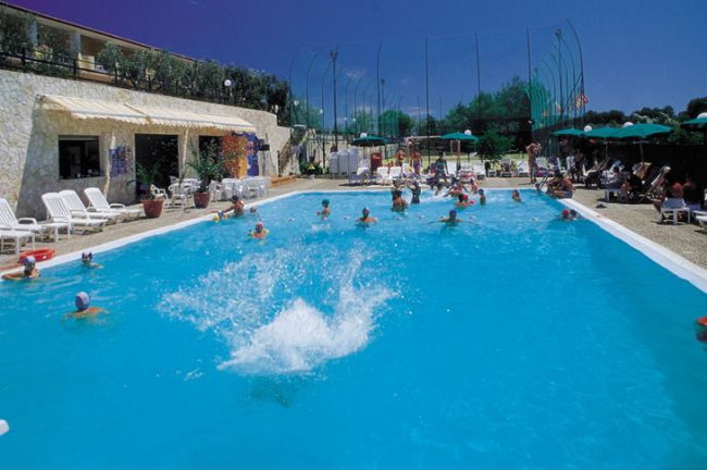 Piscina con persone che nuotano, ombrelloni verdi nelle vicinanze.