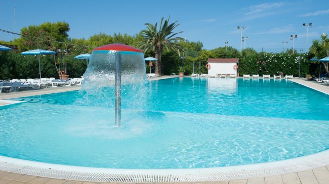 Piscina con fontana e lettini bianchi.